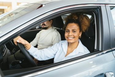 Smiling woman sitting in the driver’s seat of a car with a passenger beside her